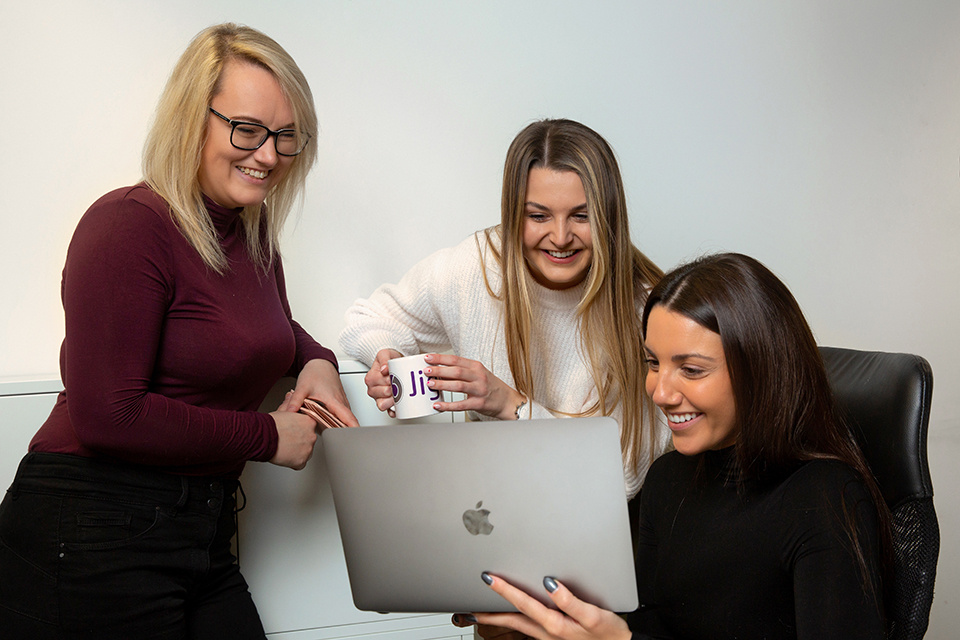 three women look at a laptop and smile 