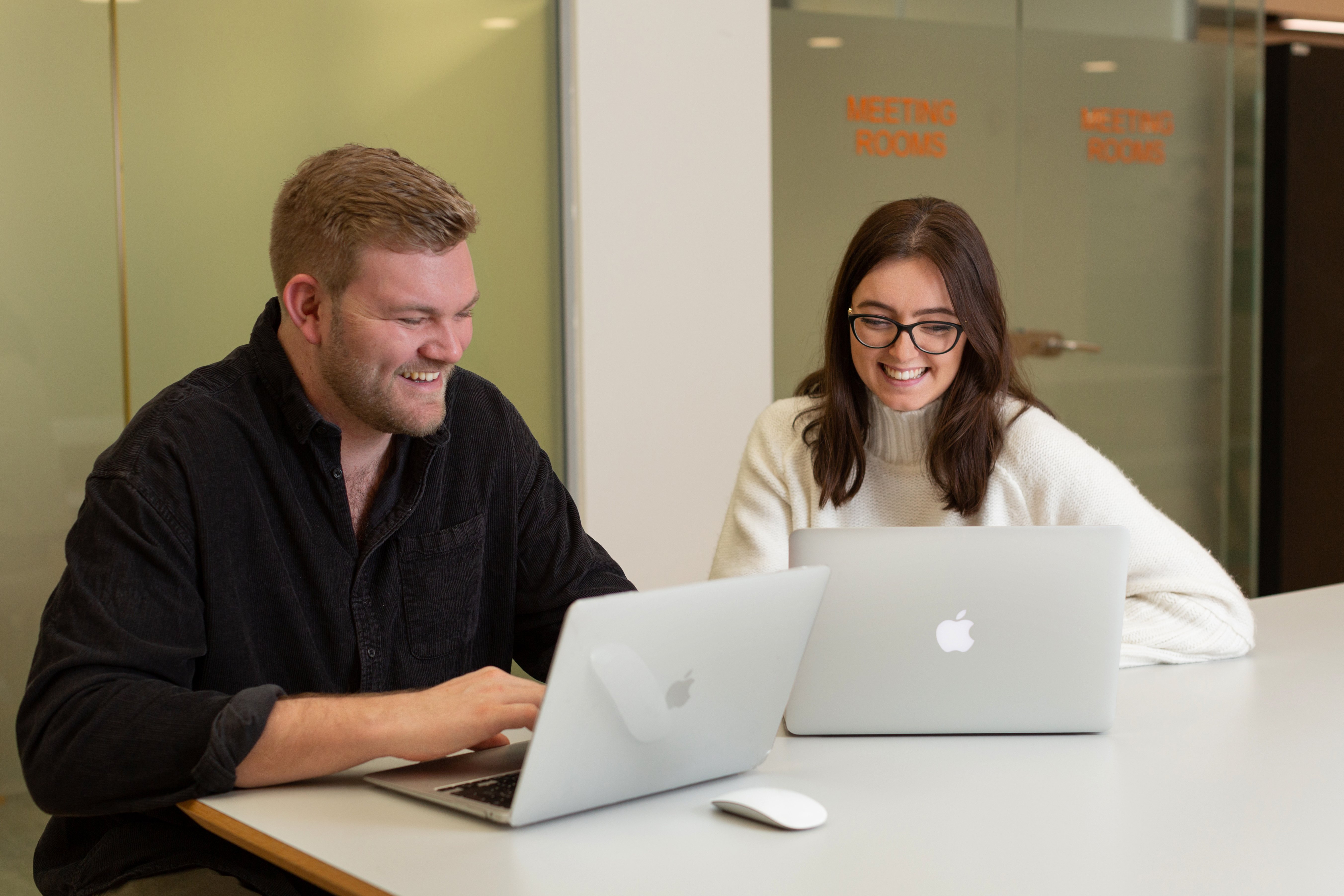 Two people sit at a table on their laptops working