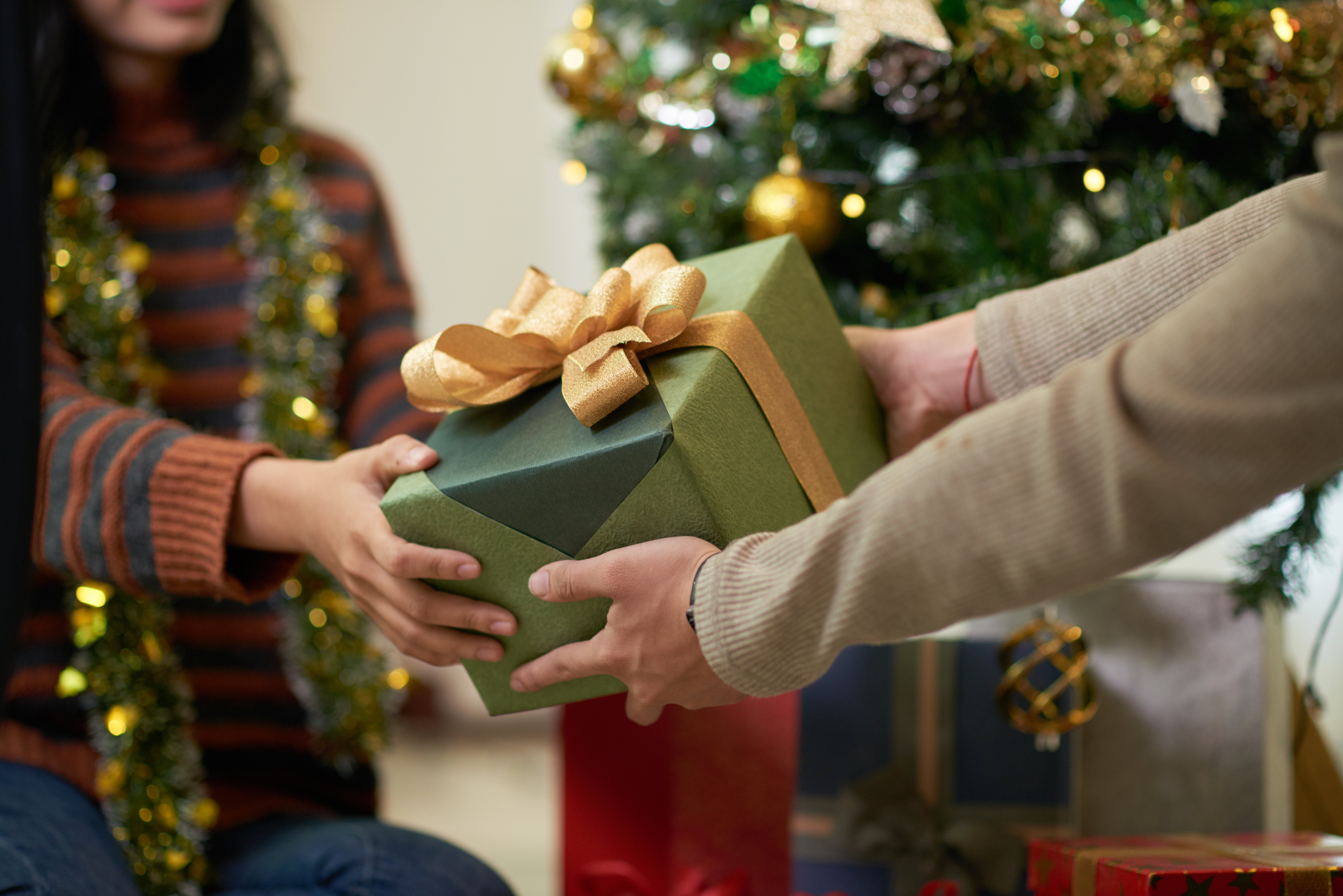 Two people pass a present, wrapped in green paper with a gold bow between them