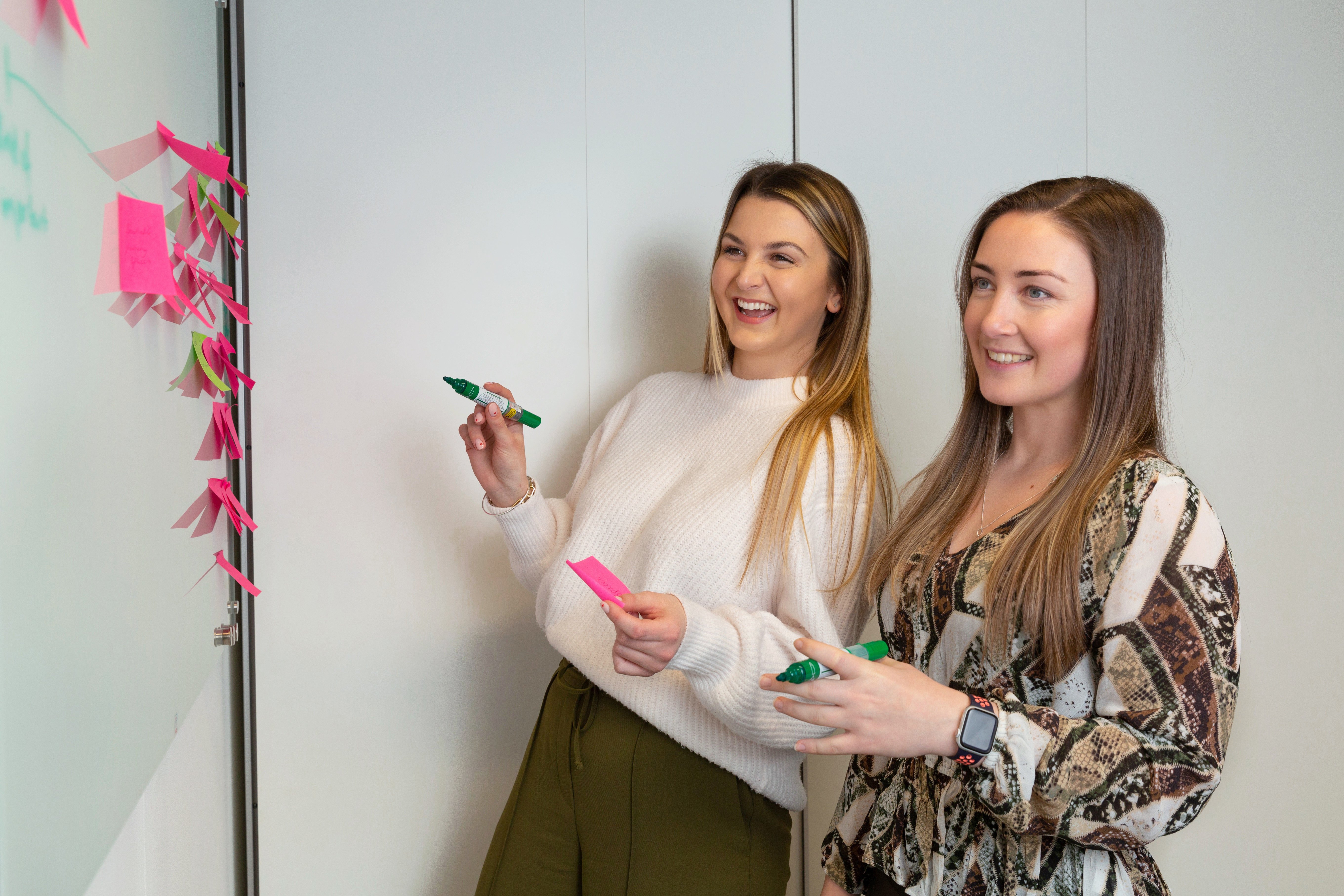 Niamh and Ocean smile as they add post-it notes to a whiteboard